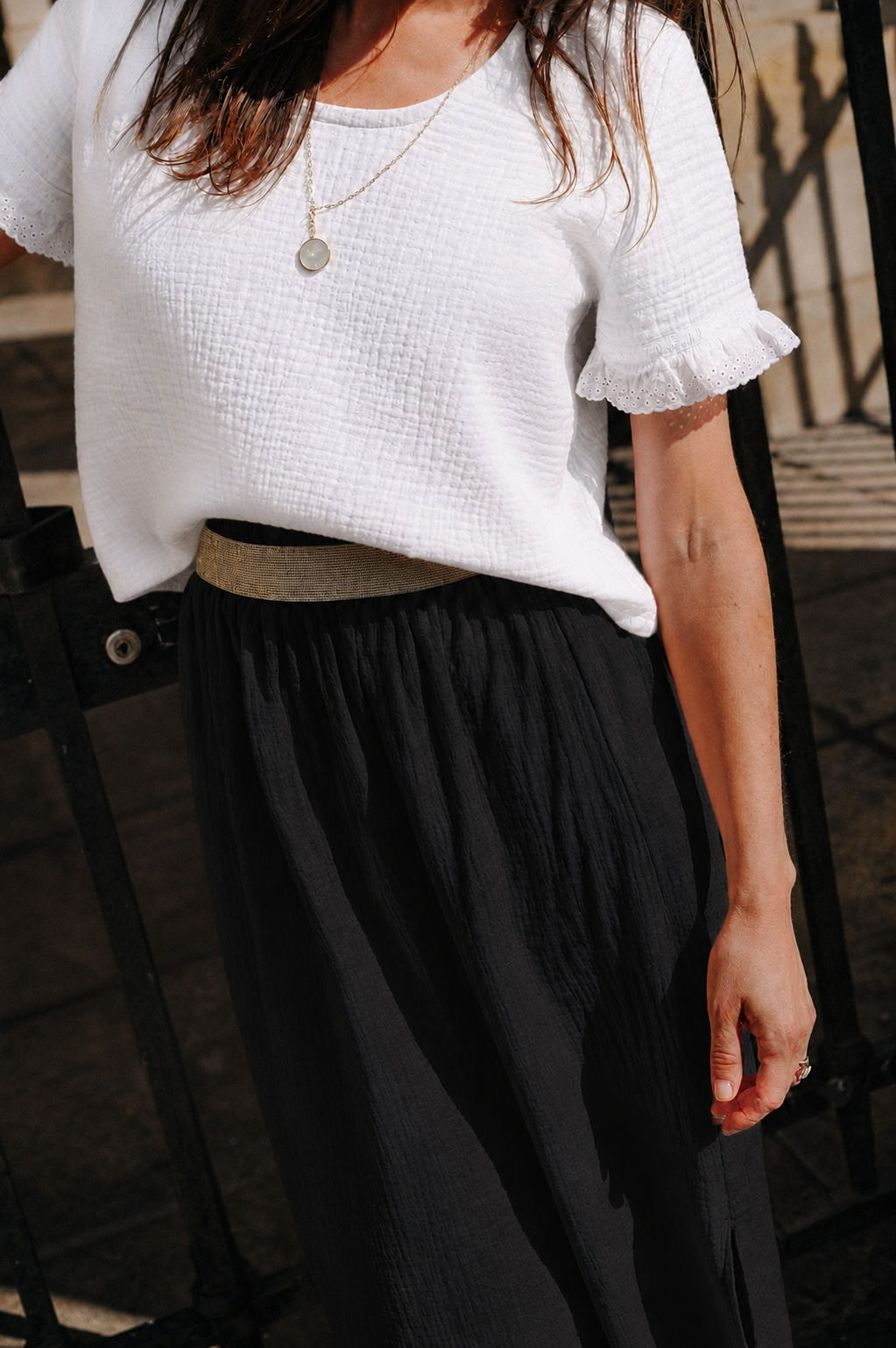 Taille élastiquée de la jupe Lison noire portée avec une ceinture dorée et un top blanc